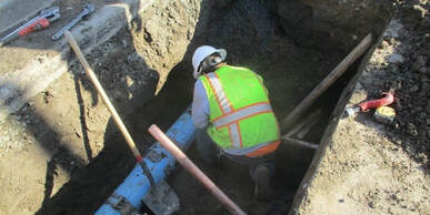 Construction worker bent down looking at underground pipe