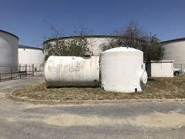 Large white tanks with two smaller tanks in front. One small tank is on its side