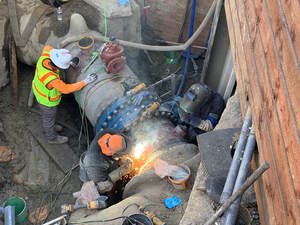 Large pipe with two construction workers, one welding and the other with his hands on the pipe